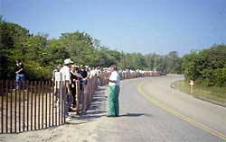 photo showing a crowd of spectators queued behind a temporary snow fence, and an official standing on the other side of the fence near the beginning of the queue