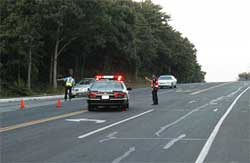 photo showing a police cruiser parked in the middle of a two-lane arterial, and two traffic control officers directing traffic to turn onto an alternate route