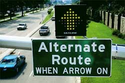 photo showing a dynamic blank-out sign, mounted on a mast arm above a sign stating "alternate route – when arrow on," displaying a pull-through arrow