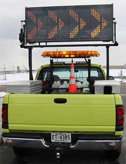a photo showing a changeable message sign over a pick-up truck shown from the rear, containing various equipment in its bed