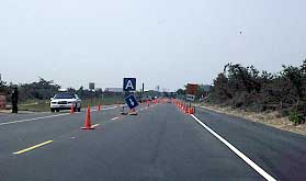 photo showing a two-lane arterial that is coned and signed for temporary four-lane operation using the road shoulders