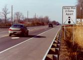 photo of roadway with car traveling over large white dots in lane; sign to right of roadway shows the words "keep min 2 dots apart"