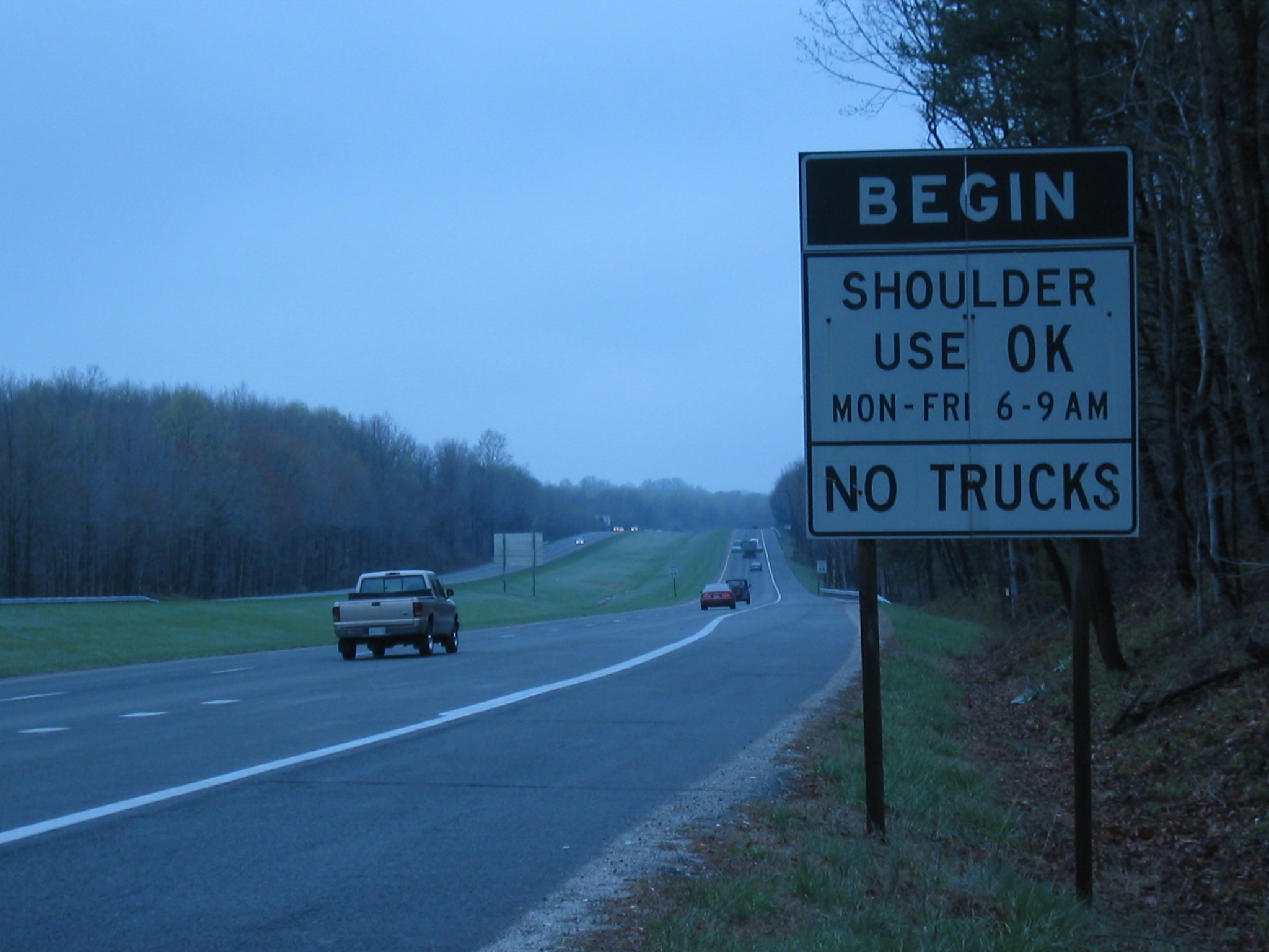photo showing sign to the right of a roadway with the words "Begin shoulder use OK, Mon-Fri 6-9 AM, no trucks"