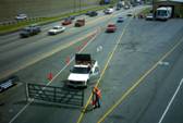 Photograph:    Freeway exit ramp that is closed with a manual gate.  An operator is standing near near the gate.  The operator's vehicle is parked immediately in front of the gate.  