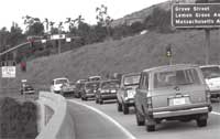 Photograph - A three-lane metered entrance ramp.  Vehicles are queued in each lane.  A sign posted on the left side of the ramp states: Left Lane Carpools 2 or More Only.