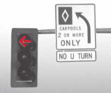 Photograph - Close up of a traffic signal mast arm.  Attached to the mast arm is a sign that reads Carpools 2 or More Only.  Beneath this sign is another sign that states No U Turn.