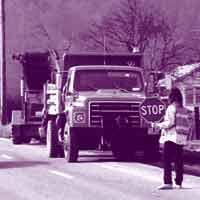 Construction worker on a roadway holds a stop sign. One truck is traveling on the road.