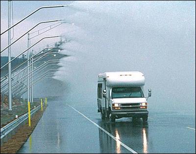 This figure presents a photograph of a vehicle driving on a roadway with elevated mechanisms spraying water onto the roadway environment.