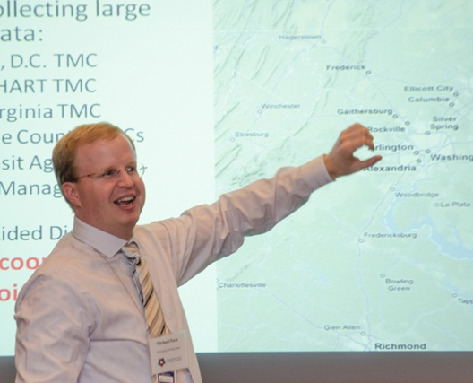 Photograph of Michael Pack pointing to a section of a map on a projection screen during his presentation
