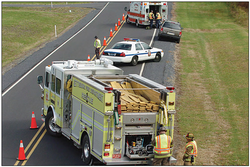 Photo of a fire truck parked on a roadway at an angle behind a police car, which is angled behind a disabled vehicle and an emergency medical vehicle