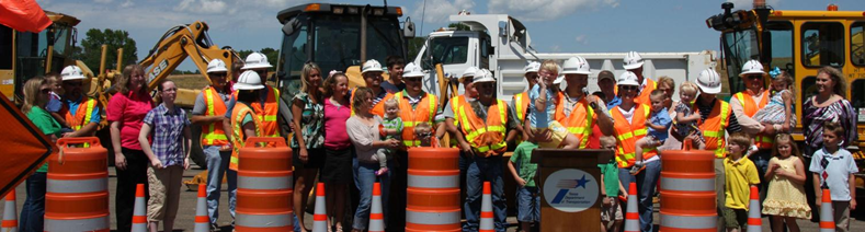 Road workers and their families behind orange barrels at a work zone safety event.