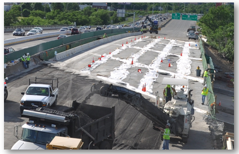 The completely installed bridge deck with workers preparing to lay asphalt over the new structure.
