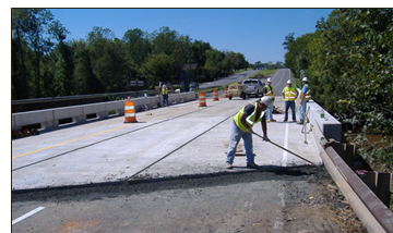 Workers placing asphalt at the abutment and sealing the deck joints.