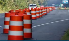 Traffic barrels delineate a stretch of newly laid asphalt in a rural work zone.