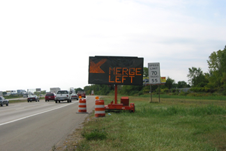 A dynamic message sign in a work zone displaying 'Merge Left'.