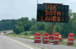 A dynamic message sign in a work zone displaying 'Use Both Lanes'.