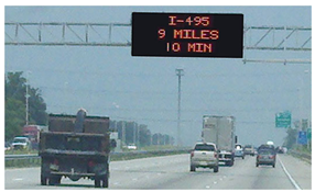 Image of a roadway with a changable message sign displaying travel timemounted on an overhead gantry.