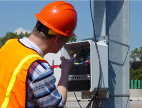 A workers setting up a detector that has been mounted on a roadside structure.
