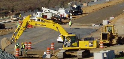 Photo of a large backhoe digging up part of a highway, and other construction vehicles on the side of the road