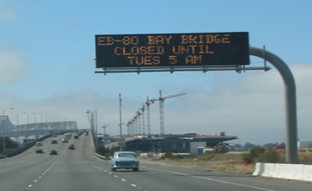 Photo of sign to right of highway with the message "EB-80 Bay Bridge Closed Until Tues 5 AM"