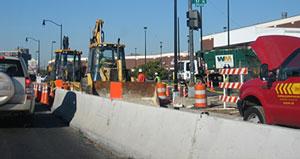 Photo of concrete barriers between traffic in a travel lane and equipment and workers in a work zone lane.