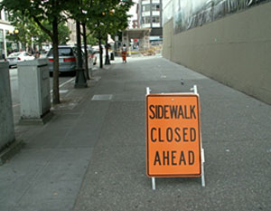 Photo of a Sidewalk Closed Ahead warning sign in the middle of a sidewalk.