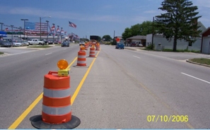 Photo of a roadway with opposing traffic separated by work zone barrels down the narrow median area.