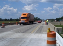 photo of a reconstructed overpass with yellow barrels along the sides of the roadway on the shoulder area.