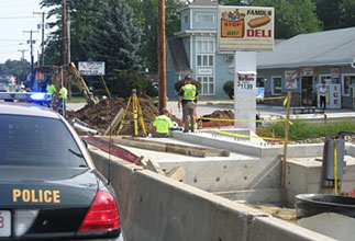 Photo of a New Hampshire State Police cruiser next to a work zone, with a uniformed police officer wearing a yellow-green safety vest standing next to a worker in a yellow-green safety shirt.