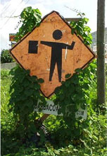 Photo of a battered flagger symbol warning sign with vines covering part of the sign.