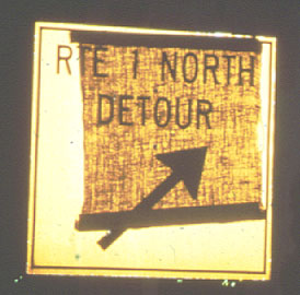Photo of a Rte 1 North Detour sign covered with a piece of burlap, with the message showing through the burlap.