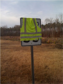 Photo of a speed limit sign covered by a yellow-green safety vest, which obscures the listed speed limit.