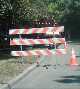 Photo of a Type III barricade on a roadway, with the diagonal stripes on the top rail pointing in the opposite direction of those on the lower two rails.