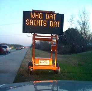 Photo of a portable changeable message sign next to a roadway displaying the message "Who Dat Saints Dat."