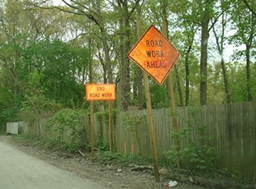 Photo of a Road Work Ahead warning sign immediately in front of an End Road Work sign next to a roadway.