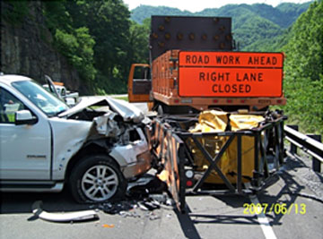 Photo of a car crashed into a truck mounted attenuator and a Road Work Ahead: Right Lane Closed warning sign.