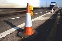 Photo of an orange and white striped traffic cone with a mounted warning light.