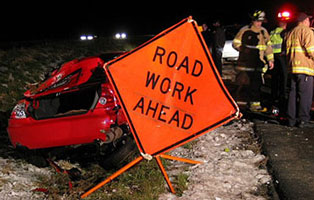 Photo of a car crashed into a bent Road Work Ahead warning sign.