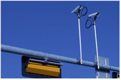 A photograph shows two cameras mounted on a fixture that includes road signage and a traffic signal box.