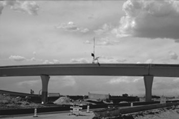 Figure 1 - This figure shows sensor equipment, powered by a solar panel and communicating via wireless means. The sensor is placed on an overpass above a mainline route that is under construction. A lane closure sign is directing drivers to merge left on the mainline.