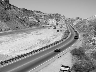 This figure shows a stretch of State Route 68 while construction is under way. Vehicles are traveling up the steep grade of the existing roadway, while the parallel roadway is being constructed on the other side of a wide median. Construction vehicles are scattered throughout the median, and the roadway and construction area are surrounded by mountains.